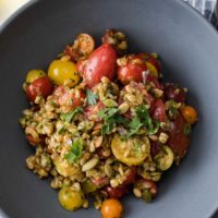 Overhead, close-up shot of a grain salad made with cooked farro, fresh grape tomatoes, and green harissa.