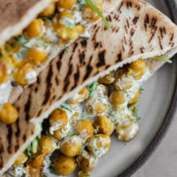 Close-up overhead shot of chickpea curry stuffed in pita with a dill yogurt sauce and arugula.