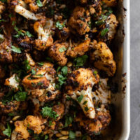 Overhead shot of cauliflower on a sheet tray, tossed and roasted with mole sauce.