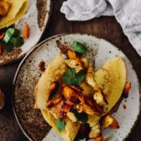 Overhead photo, close-up, of yellow chickpea crepes topped with parsnip and carrot pieces and chipotle compound butter