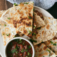 Overhead photograph of quesadillas on a white plate with a small white bowl of red salsa.