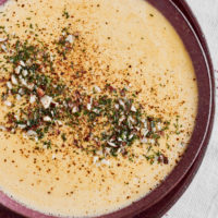 Close-up photograph of sweet corn soup with a dill garnish in a dark pink bowl.