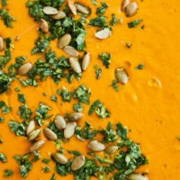 Close-up photo of orange carrot soup topped with cilantro and green pepitas.