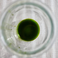 Top-down image of a clear jar on a white linen surface with green parsley oil.
