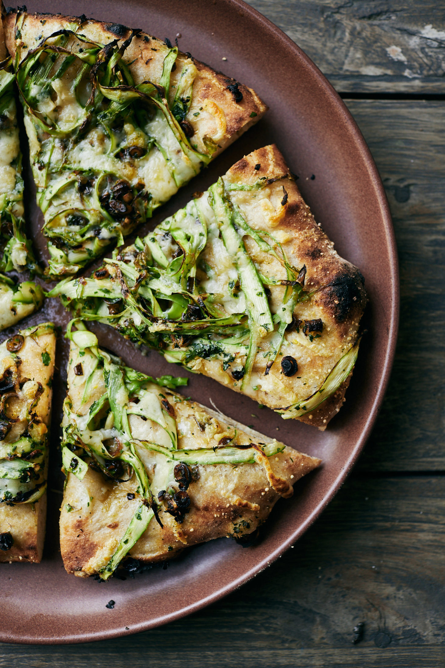 Close-up of asparagus pizza cut into pieces on a red plate.