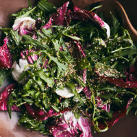 close-up of a brick colored bowl filled with arugula, radicchio, and sesame seeds.