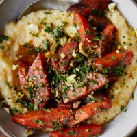 Close-up image of a white bowl with polenta and topped with orange braised carrots.
