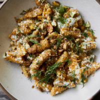 Close-up photo of orange cavatelli in a white bowl topped with ricotta and dill.