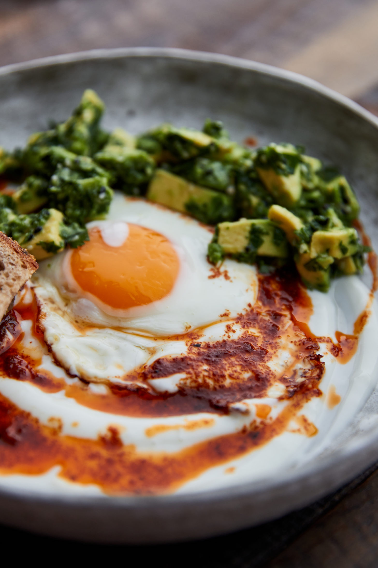 Close-up, side-angle photograph of a sunny-side up egg on top of yogurt in a grey-white bowl.
