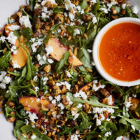 Close-up photo of a salad with peaches, pistachios, a chili dressing- all in a grey bowl.