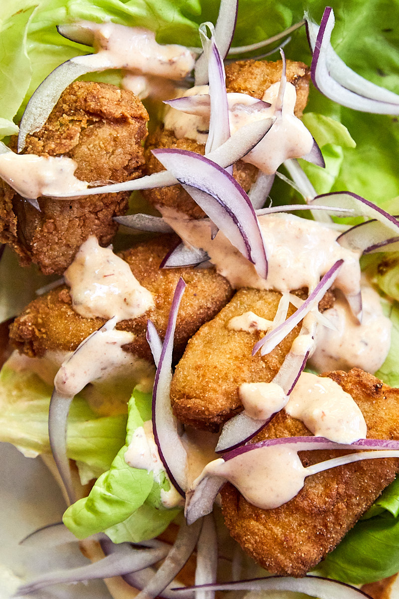Close-up photo of fried green tomato in a wrap with lettuce, slices of onions and a chipotle sauce drizzle on top.