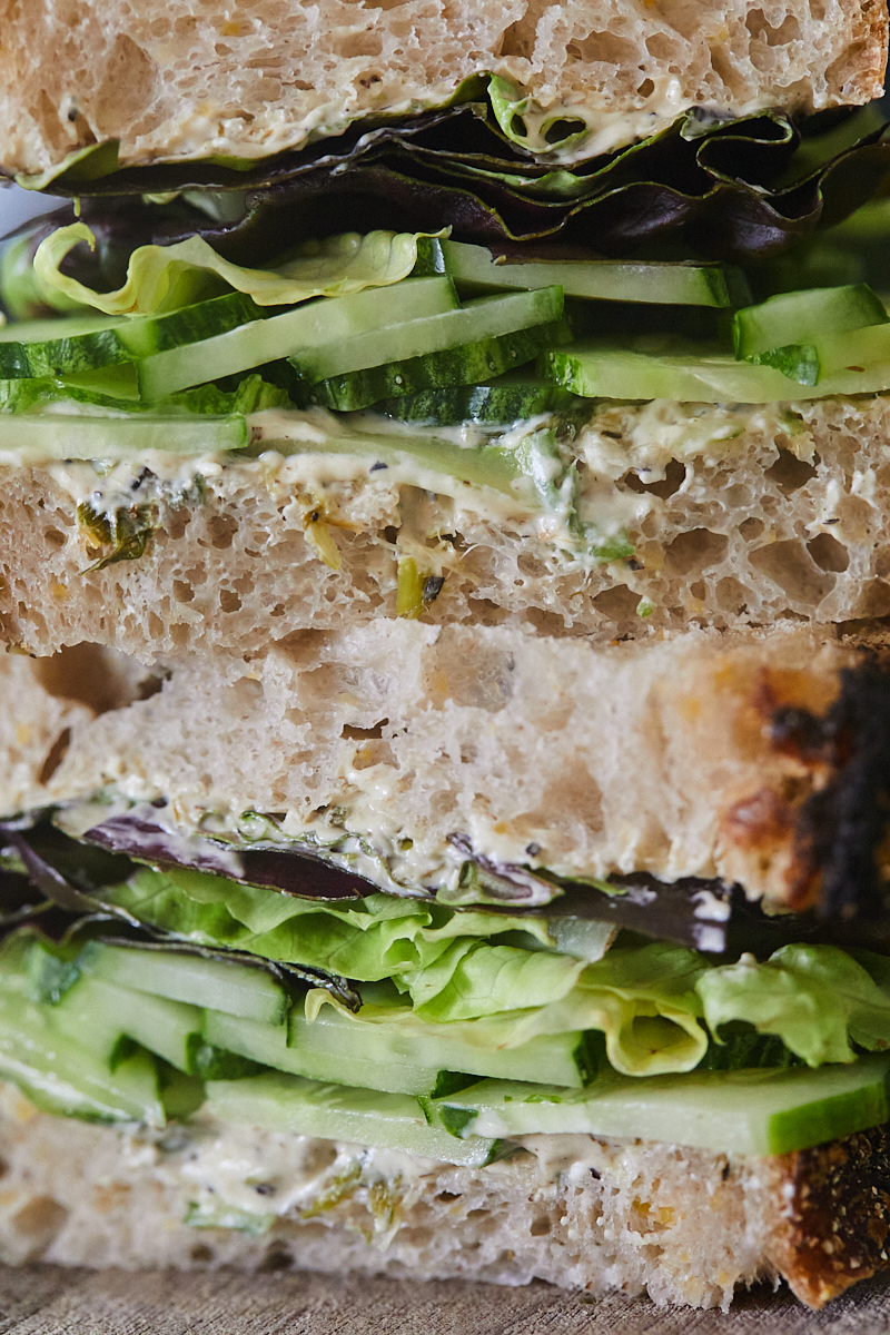 Close-up of a cucumber sandwich with layers of cucumbers, lettuce, scallion cream cheese, and bread.