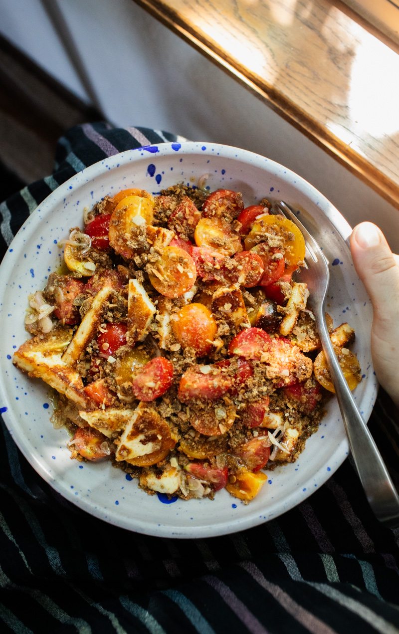An overhead photo of a tomato halloumi salad in a white bowl with blue speckles.
