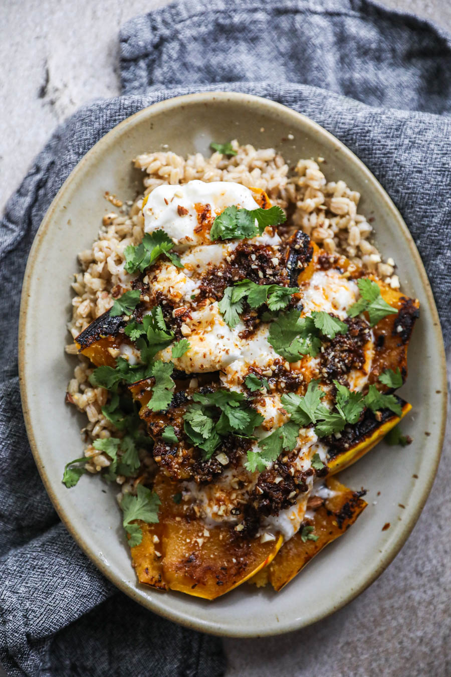 A tan platter with blue napkin that holds barley topped with delicata squash, chile butter, and cilantro.